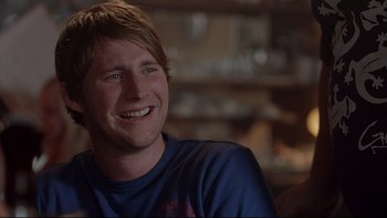 Movie still from “Hostel” (2005), directed by Eli Roth – A man smiling while sitting in front of a window; Close Up shot, Over the shoulder angle