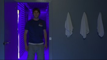 Movie still from “Hostel” (2005), directed by Eli Roth – A man standing in a room with a blue light; Medium shot, Low angle