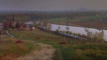 Movie still from “Hostel” (2005), directed by Eli Roth – A train traveling down tracks next to a body of water; Extreme Wide shot, High angle