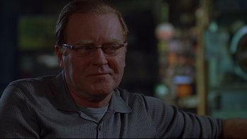 Movie still from “Hostel” (2005), directed by Eli Roth – A person wearing glasses and a gray shirt; Close Up shot, Over the shoulder angle