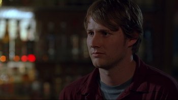 Movie still from “Hostel” (2005), directed by Eli Roth – A man in a red shirt is looking to his left; Close Up shot, Over the shoulder angle