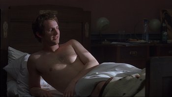 Movie still from “Hostel” (2005), directed by Eli Roth – A man laying in a bed with his shirt off; Medium shot, High angle
