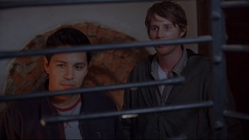 Movie still from “Hostel” (2005), directed by Eli Roth – Two young men standing next to each other in front of a fence; Medium shot, Low angle