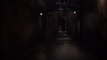 Movie still from “Hostel” (2005), directed by Eli Roth – A person walking in a dark hallway with lights on; Extreme Wide shot, High angle