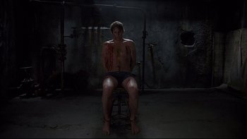 Movie still from “Hostel” (2005), directed by Eli Roth – A man sitting on a chair in a dark room; Wide shot, High angle