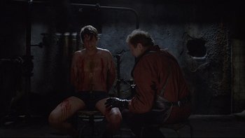 Movie still from “Hostel” (2005), directed by Eli Roth – A man is sitting on a chair with blood on his chest; Medium shot, Over the shoulder angle