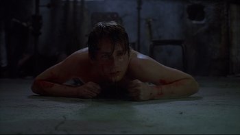 Movie still from “Hostel” (2005), directed by Eli Roth – A man laying on the ground with blood all over his body; Medium shot, High angle