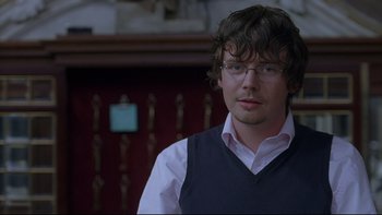 Movie still from “Hostel” (2005), directed by Eli Roth – A man wearing glasses and a vest looking at the camera; Close Up shot, Over the shoulder angle