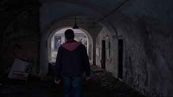 Movie still from “Hostel” (2005), directed by Eli Roth – A man standing in an arched hallway looking out the window; Wide shot, Over the shoulder angle