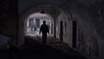 Movie still from “Hostel” (2005), directed by Eli Roth – A man walking through an archway in a building; Wide shot, Over the shoulder angle