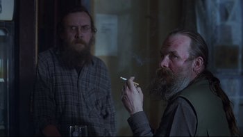 Movie still from “Hostel” (2005), directed by Eli Roth – A man smoking a cigarette in front of another man; Medium shot, Over the shoulder angle
