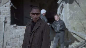 Movie still from “Hostel” (2005), directed by Eli Roth – A man wearing sunglasses standing in front of two other men; Medium shot, Over the shoulder angle