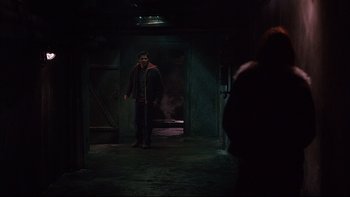Movie still from “Hostel” (2005), directed by Eli Roth – A man standing in a room with smoke coming out of a door; Wide shot, Over the shoulder angle