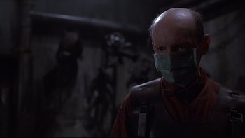 Movie still from “Hostel” (2005), directed by Eli Roth – An older man wearing a surgical face mask; Close Up shot, Over the shoulder angle