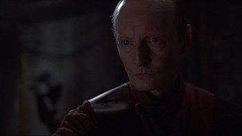 Movie still from “Hostel” (2005), directed by Eli Roth – An old man with a bald head and a goatee looking at the camera; Close Up shot, Over the shoulder angle