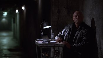 Movie still from “Hostel” (2005), directed by Eli Roth – A man sitting at a table in a dark room; Medium shot, Low angle