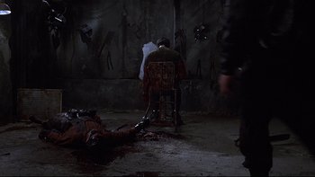 Movie still from “Hostel” (2005), directed by Eli Roth – A man sitting in a chair next to a dead body; Wide shot, High angle