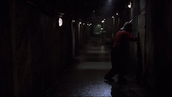 Movie still from “Hostel” (2005), directed by Eli Roth – A man in a red shirt is walking in a dark hallway; Wide shot, High angle