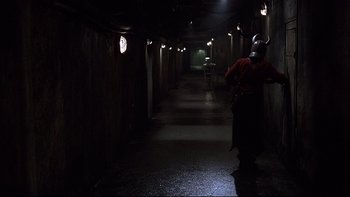 Movie still from “Hostel” (2005), directed by Eli Roth – A man in a helmet is standing in a dark hallway; Wide shot, High angle