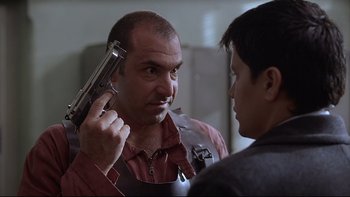 Movie still from “Hostel” (2005), directed by Eli Roth – A man holding a gun up to his head while another man looks at him; Close Up shot, Over the shoulder angle