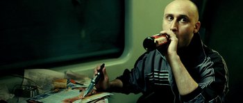 Movie still from “Hostel: Part II” (2007), directed by Eli Roth – A bald man holding a knife and drinking a beer; Medium shot, High angle