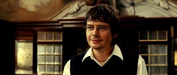 Movie still from “Hostel: Part II” (2007), directed by Eli Roth – A man wearing glasses and a sweater vest is smiling; Close Up shot, High angle