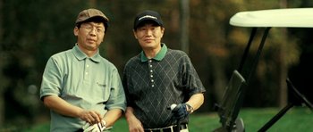 Movie still from “Hostel: Part II” (2007), directed by Eli Roth – A couple of men standing next to each other on top of a golf course; Medium shot, Low angle