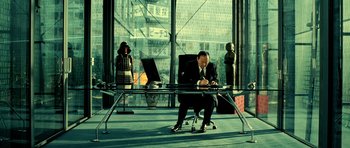 Movie still from “Hostel: Part II” (2007), directed by Eli Roth – A man sitting at a desk in front of a woman; Wide shot, High angle