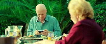 Movie still from “Hostel: Part II” (2007), directed by Eli Roth – An older man sitting at a table looking at his cell phone; Medium shot, High angle