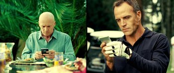 Movie still from “Hostel: Part II” (2007), directed by Eli Roth – Two men sitting at a table and one of them is using a cell phone; Close Up shot, Low angle