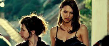 Movie still from “Hostel: Part II” (2007), directed by Eli Roth – A woman in a black top is standing next to another woman in a black dress; Close Up shot, Over the shoulder angle
