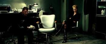 Movie still from “Hostel: Part II” (2007), directed by Eli Roth – A woman sitting in front of a chair in a room; Wide shot, Over the shoulder angle