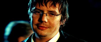 Movie still from “Hostel: Part II” (2007), directed by Eli Roth – A person wearing glasses and a suit; Close Up shot, Over the shoulder angle