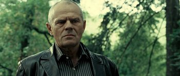 Movie still from “Hostel: Part II” (2007), directed by Eli Roth – An older man wearing a black jacket and a striped shirt; Close Up shot, Low angle