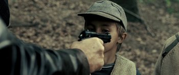 Movie still from “Hostel: Part II” (2007), directed by Eli Roth – A young boy holding a gun up to his face; Close Up shot, High angle