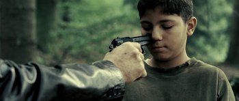 Movie still from “Hostel: Part II” (2007), directed by Eli Roth – A man holding a gun up to a young boy's face; Close Up shot, Over the shoulder angle