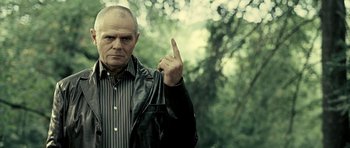 Movie still from “Hostel: Part II” (2007), directed by Eli Roth – An older man in a leather jacket is holding up a finger; Close Up shot, Low angle