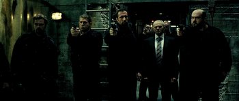 Movie still from “Hostel: Part II” (2007), directed by Eli Roth – A group of men standing next to each other holding guns; Medium shot, Low angle