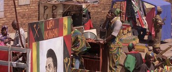 Movie still from “Hotel Rwanda” (2004), directed by Terry George – A man wearing a colorful outfit is talking on a cell phone; Medium shot, Over the shoulder angle