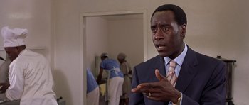 Movie still from “Hotel Rwanda” (2004), directed by Terry George – A man wearing a suit and tie talking to someone; Close Up shot, Over the shoulder angle
