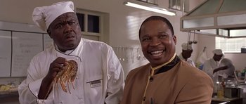 Movie still from “Hotel Rwanda” (2004), directed by Terry George – A man in a chef's hat and a man in a brown jacket smiling for the camera; Close Up shot, Low angle