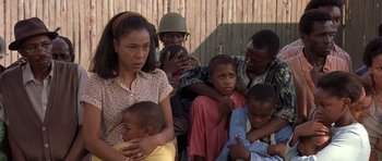 Movie still from “Hotel Rwanda” (2004), directed by Terry George – A group of people standing next to each other in front of a wooden fence; Medium shot, Over the shoulder angle