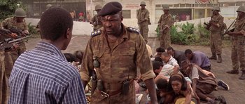 Movie still from “Hotel Rwanda” (2004), directed by Terry George – A man in a military uniform walking past a group of people; Medium shot, Over the shoulder angle