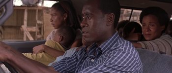 Movie still from “Hotel Rwanda” (2004), directed by Terry George – A man sitting in the back seat of a car with two other people; Close Up shot, High angle