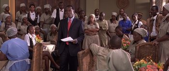 Movie still from “Hotel Rwanda” (2004), directed by Terry George – A group of people gathered around a man in a business suit; Medium shot, Over the shoulder angle