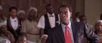 Movie still from “Hotel Rwanda” (2004), directed by Terry George – A man wearing a suit and red neck tie standing in front of other men; Close Up shot, Low angle
