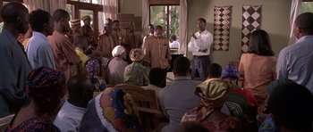Movie still from “Hotel Rwanda” (2004), directed by Terry George – A group of men standing in front of a group of people; Medium shot, Over the shoulder angle