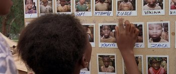 Movie still from “Hotel Rwanda” (2004), directed by Terry George – A young boy is looking at a bunch of pictures; Close Up shot, High angle