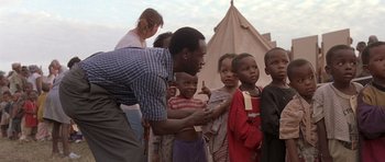 Movie still from “Hotel Rwanda” (2004), directed by Terry George – A group of people standing around each other near a tent; Medium shot, Over the shoulder angle