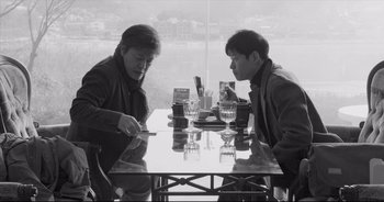 Two men are sitting at a table and one of them is holding a cell phone